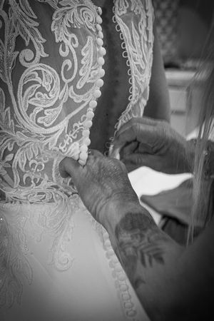 Close up black and white photo of intricate lace wedding dress details being buttoned.