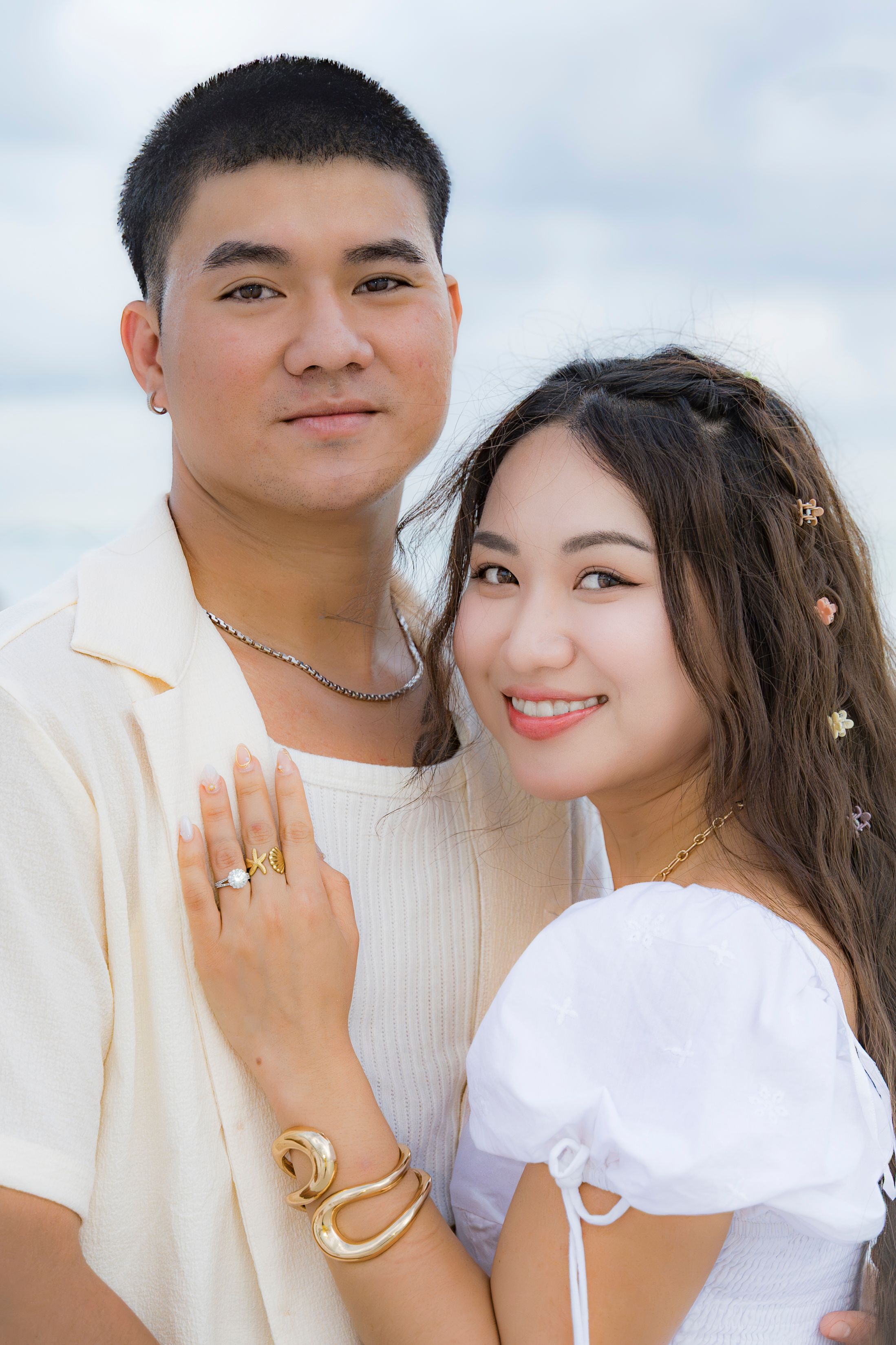 A couple wearing white outfits poses together in a romantic outdoor photoshoot.