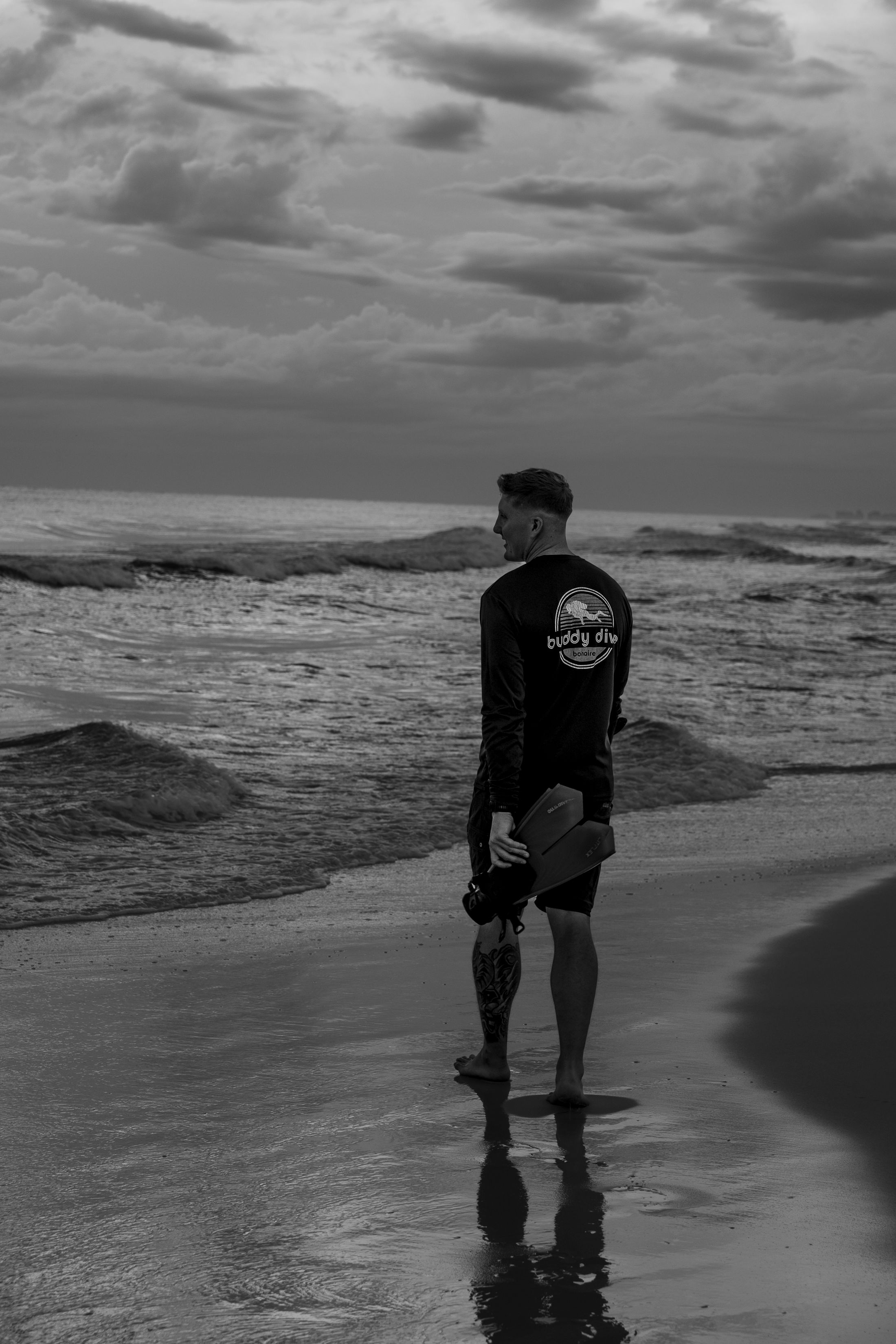 A black and white photo series shows a lone figure walking along a moody beach shoreline at sunset.