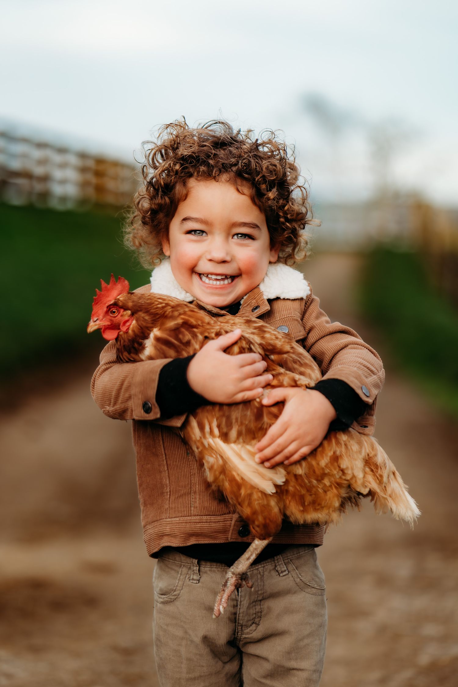A brown chicken is being hugged and held by a small child in a brown jacket.