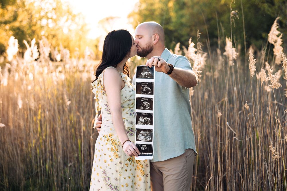 Couple kissing and holding an ultrasound pictures of their baby, Summer Outdoor Maternity Session Huntley, IL
