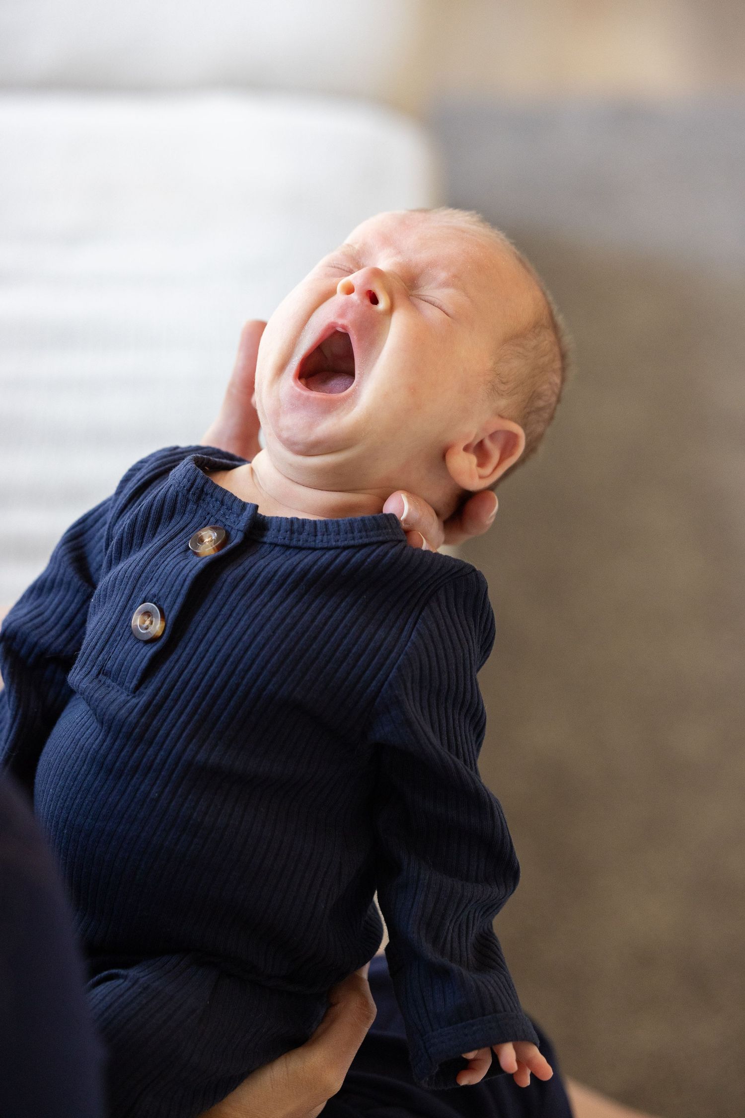 A newborn baby yawns while wearing a navy blue sweater.