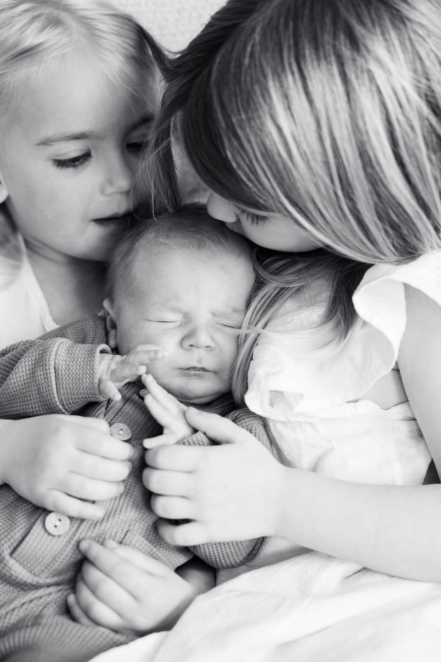 A black and white image showing a young woman tenderly holding a sleeping newborn baby, with another young child looking on affectionately.