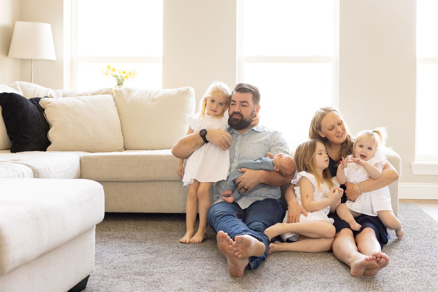 A happy family of four - a father, mother, and two young children - sitting together on a couch in a cozy living room.