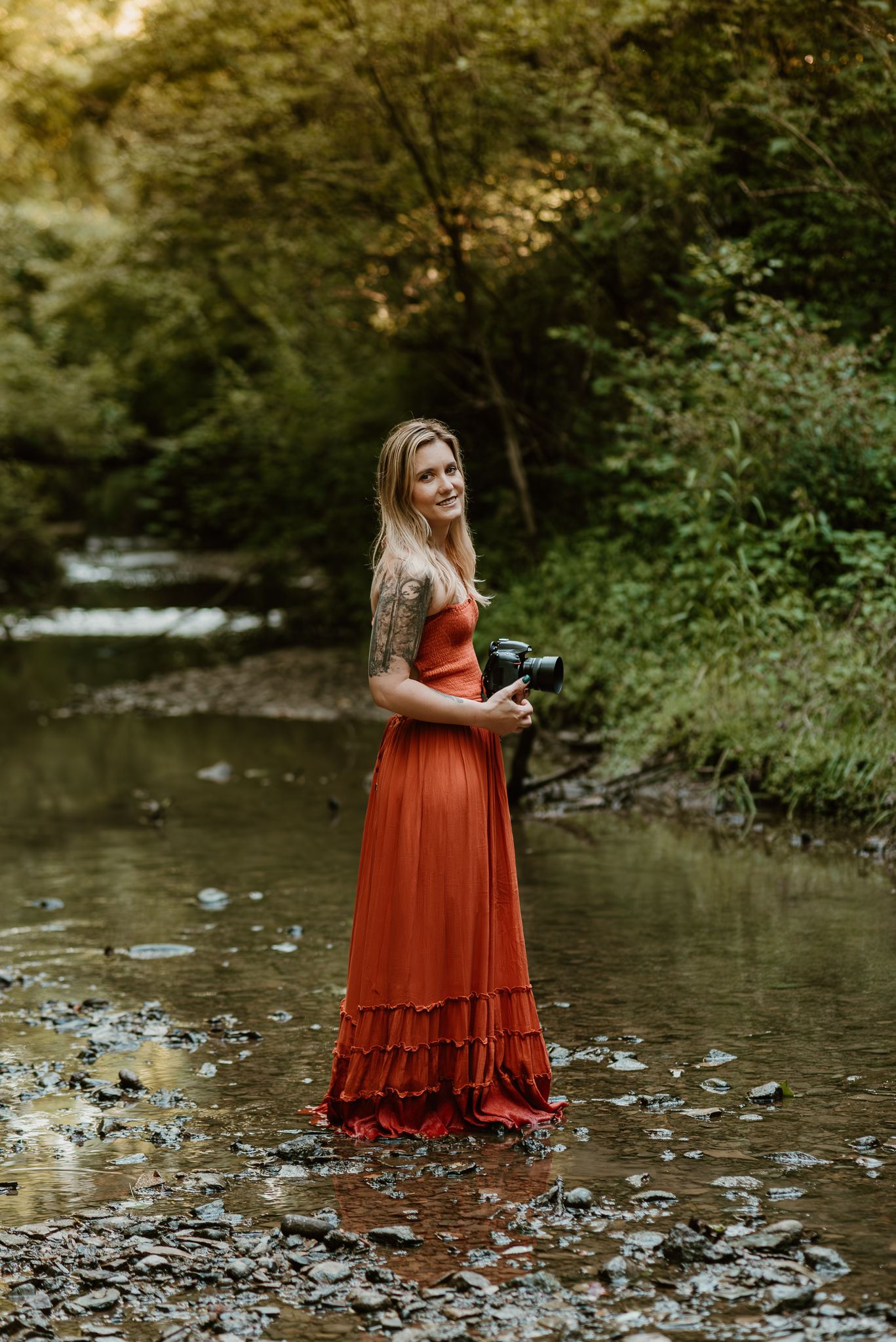 woman with tattoos and a camera, standing in creek