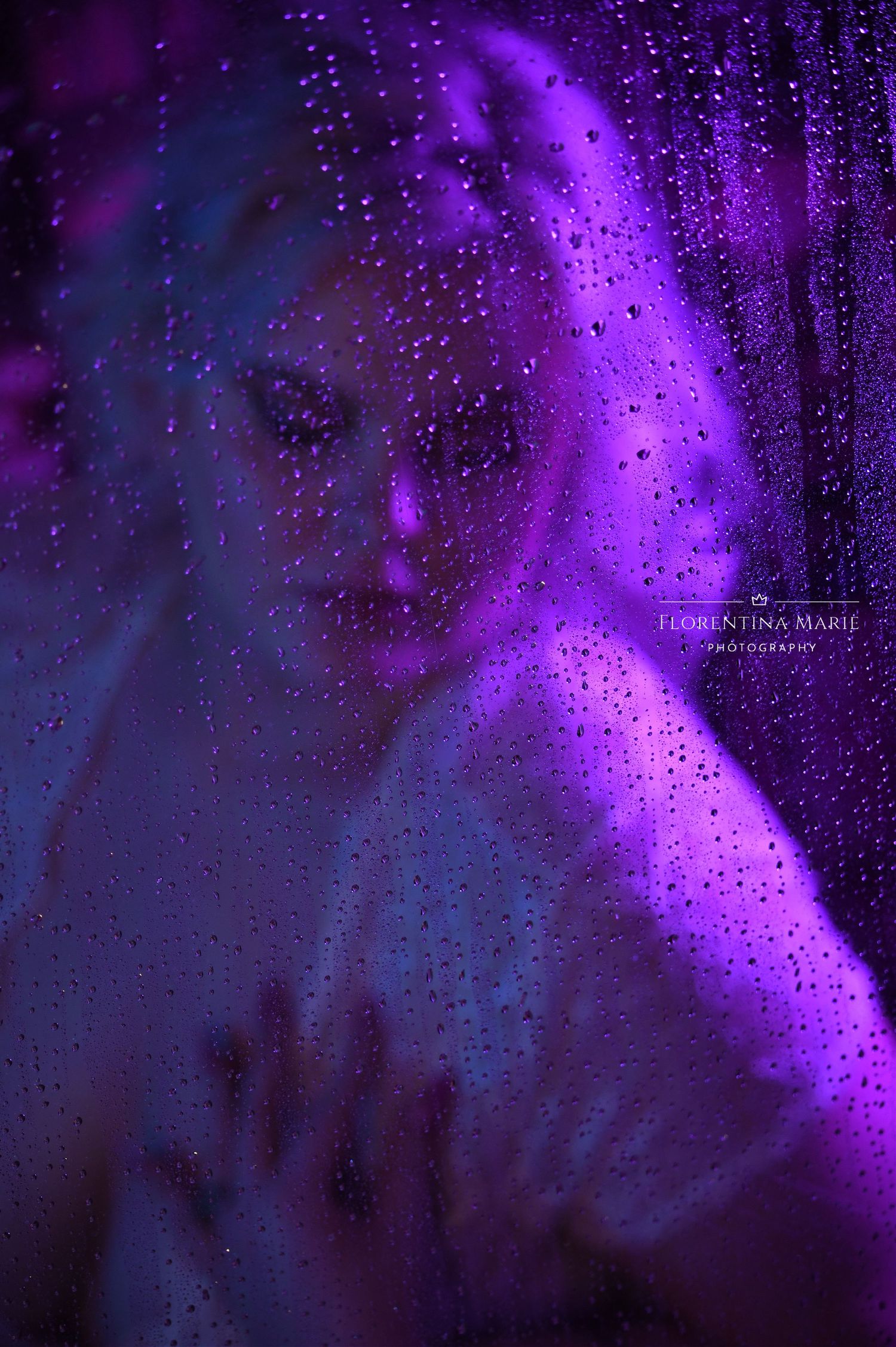 Mysterious atmospheric portrait through rainy window with vibrant purple lighting and water droplets creating ethereal effect.
