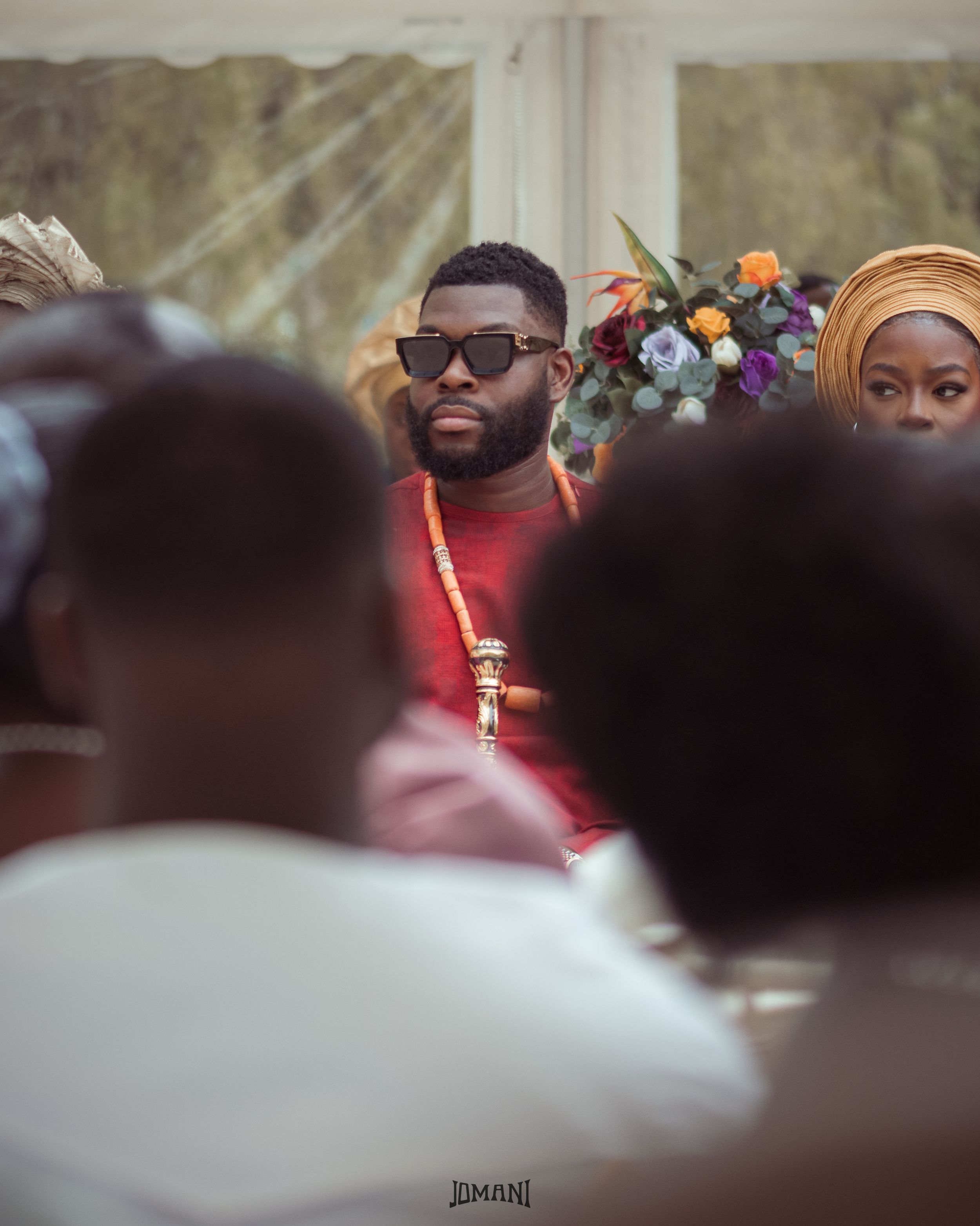 Man in red outfit and sunglasses at a traditional African wedding ceremony.