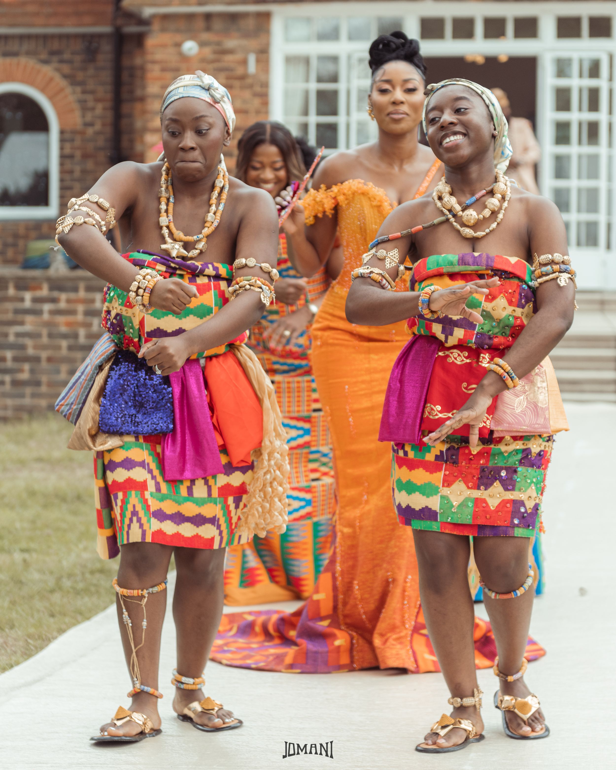 Two women dancing in colorful Kente cloth outfits at a Ghanaian traditional ceremony.