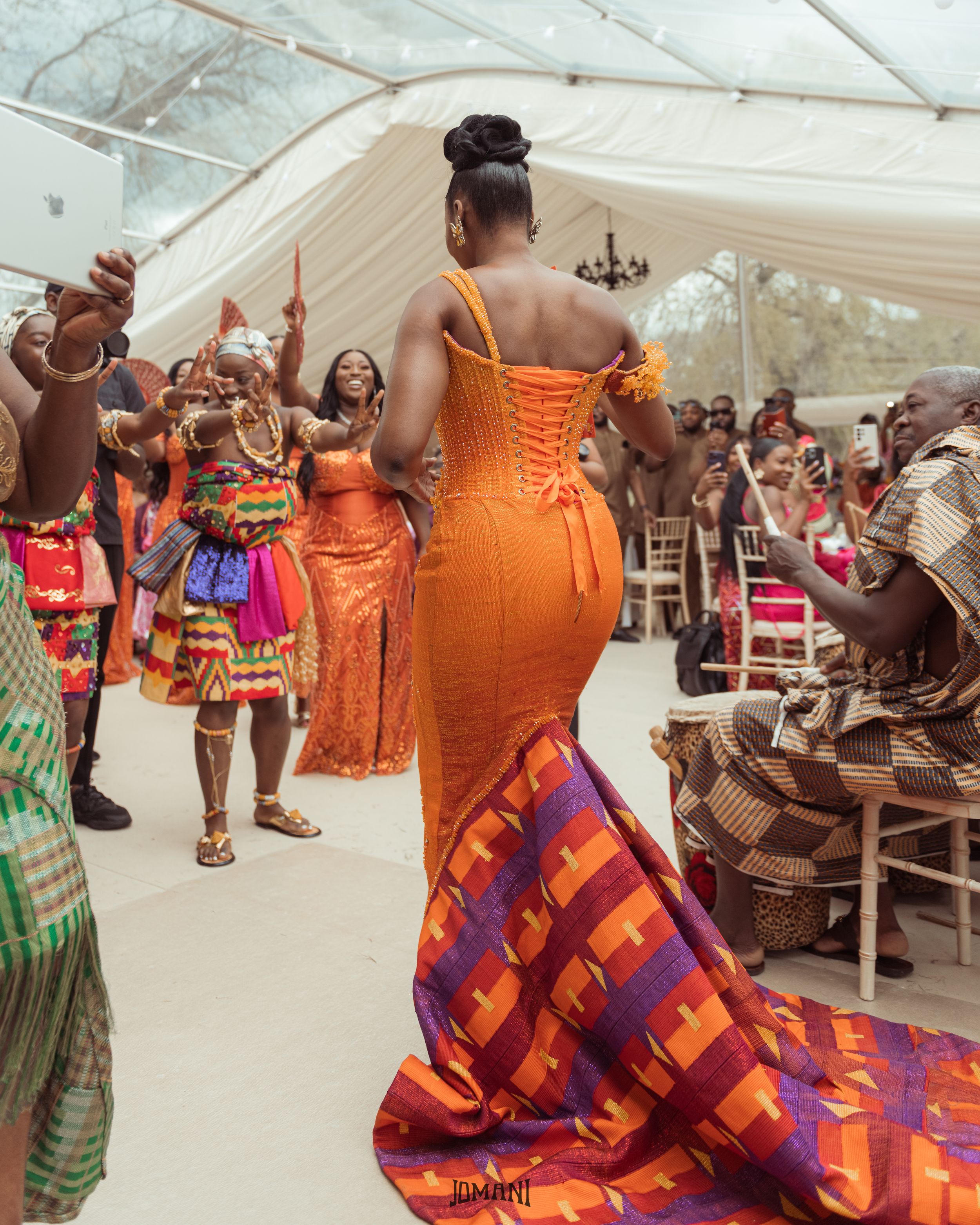 Bride in stunning orange mermaid gown dancing at a vibrant African traditional wedding.