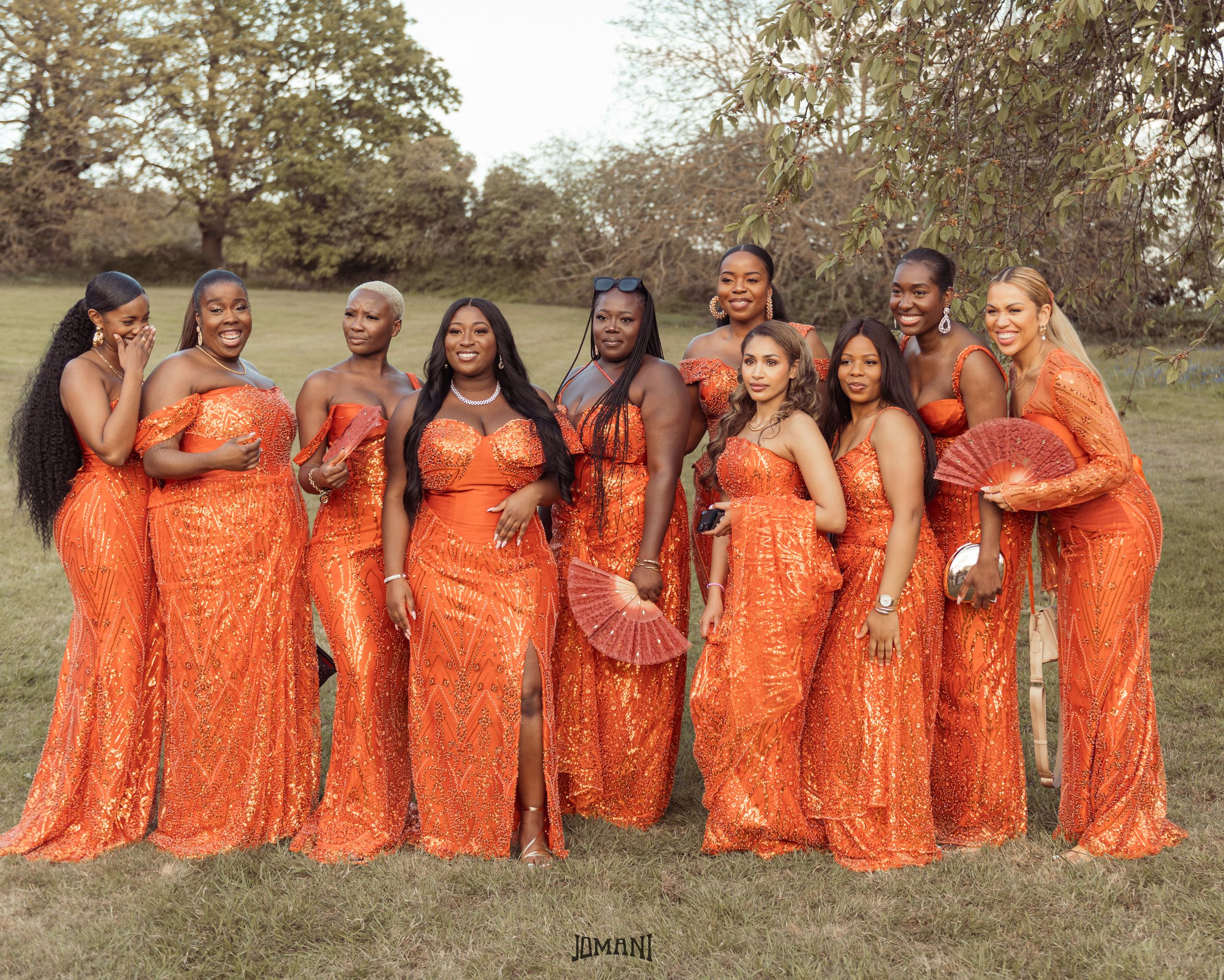 Group of bridesmaids in matching orange sequin gowns posing outdoors at a wedding.
