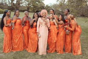 Bride surrounded by bridesmaids in orange sequin dresses laughing outdoors.