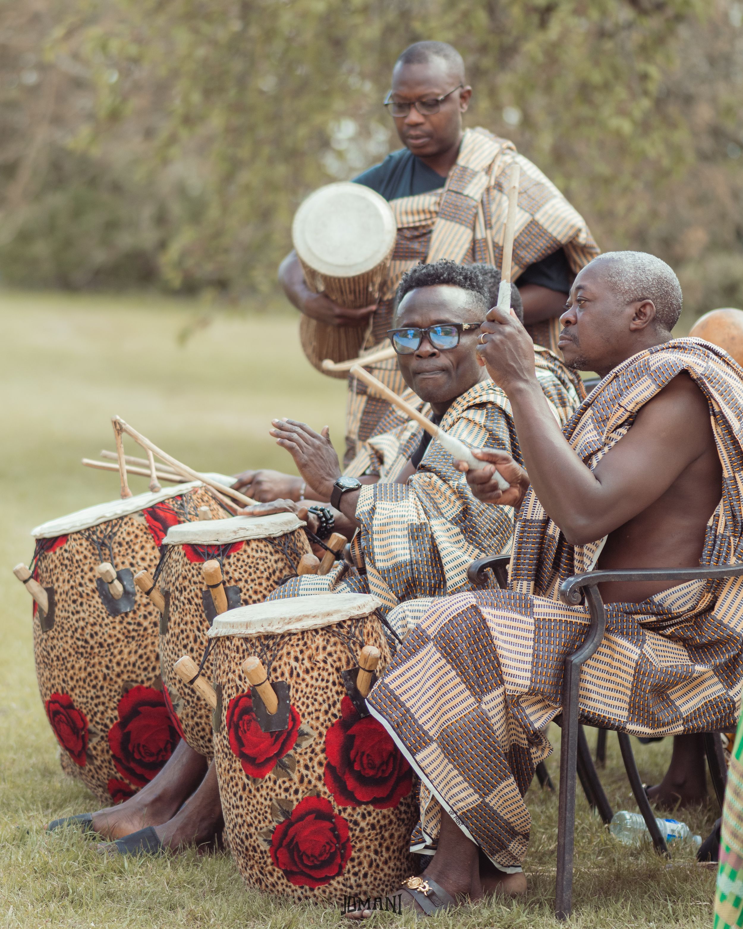 Traditional African drummers performing in patterned cloth outfits at an outdoor ceremony.