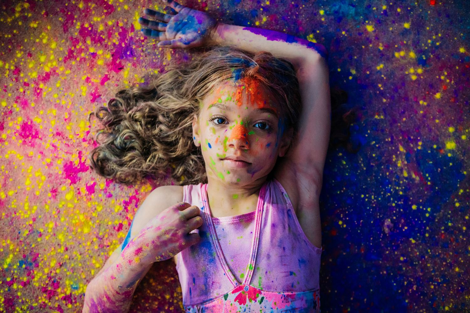 A person covered in vibrant Holi festival colors poses against a colorful powder-splattered background. Gymnast. Powder