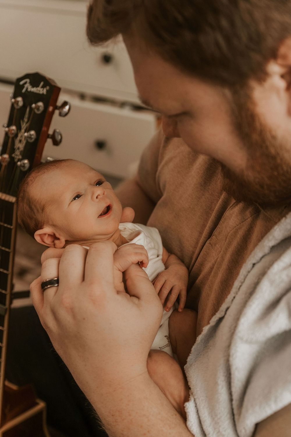 A series of tender moments between parent and baby in warm sepia tones with a guitar visible in the background.