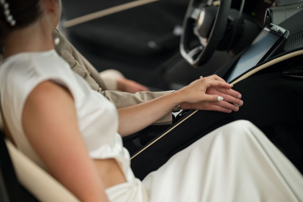 Woman in white dress sitting in luxury car interior touching touchscreen display console.