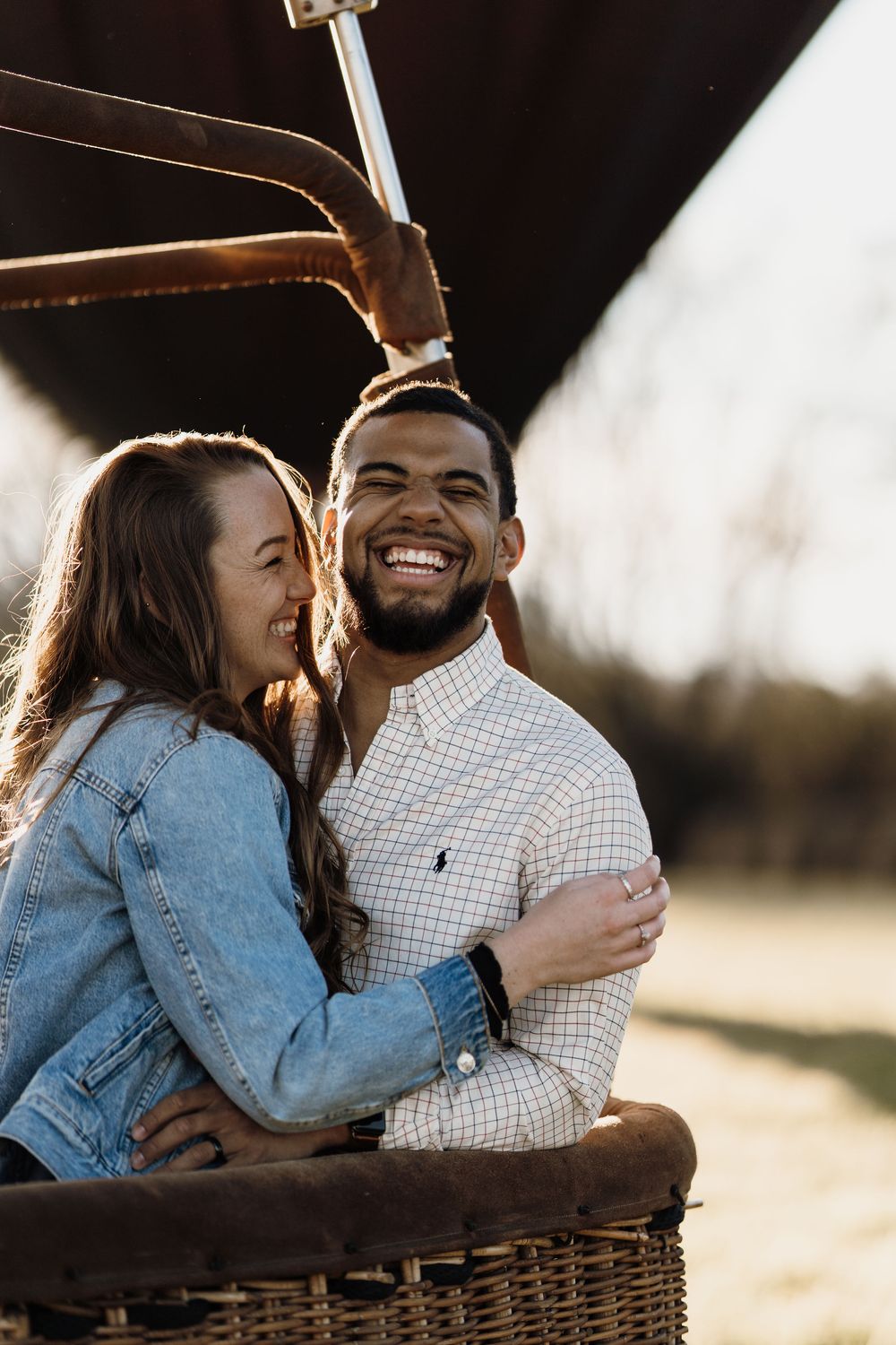 Happy couple embracing in a hot air balloon basket, smiling outdoors in warm sunlight.