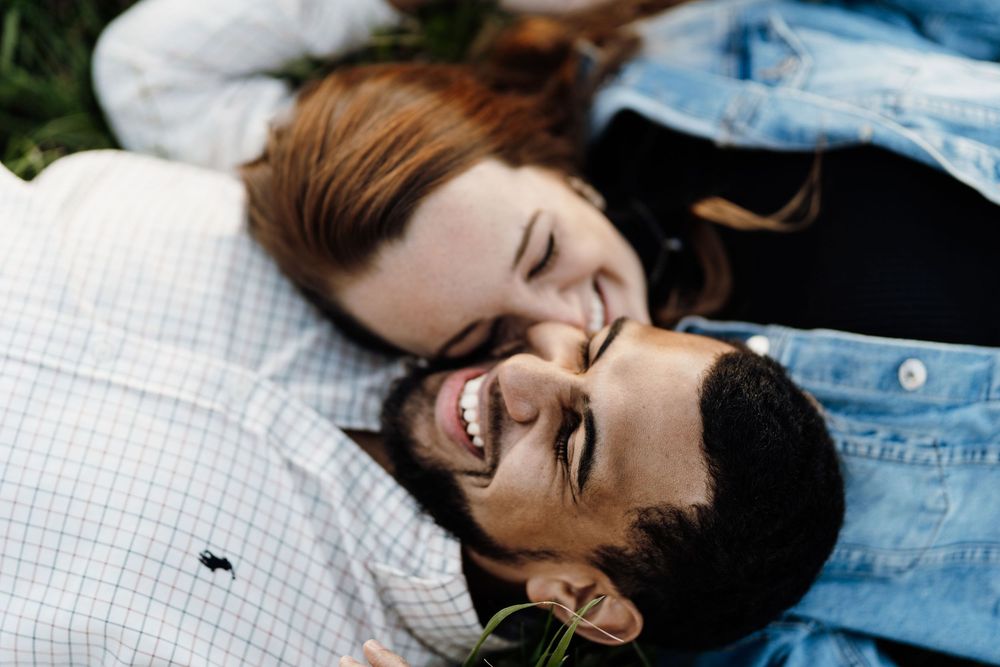 Happy couple lying on grass, laughing and smiling together in a joyful outdoor moment.