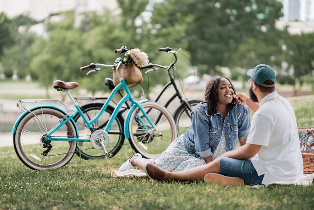 A couple enjoys a romantic picnic on green grass in a park, with two bicycles parked behind them.