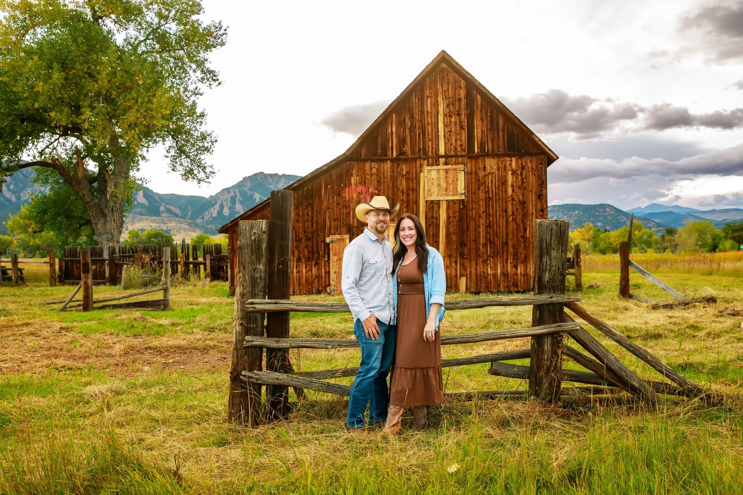Rustic wooden barn and fence set against a dramatic cloudy sky in a scenic mountain landscape.