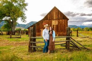 Rustic wooden barn and fence set against a dramatic cloudy sky in a scenic mountain landscape.