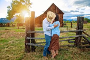 Romantic couple embracing by rustic wooden barn and fence at sunset in countryside setting.