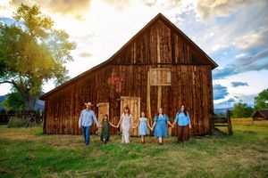 A rustic wooden barn stands against a dramatic sky as people gather outside for a photo session.