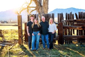 Group portrait in front of rustic wooden fence with mountains and sunset in background.