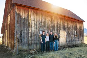 Family group portrait in front of weathered wooden barn at sunset.