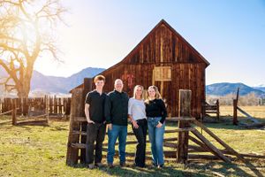 Family poses together in front of rustic wooden barn with mountain landscape in background.