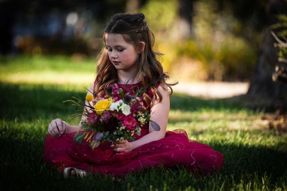 Small child in red dress sits on grass with colorful flower bouquet.