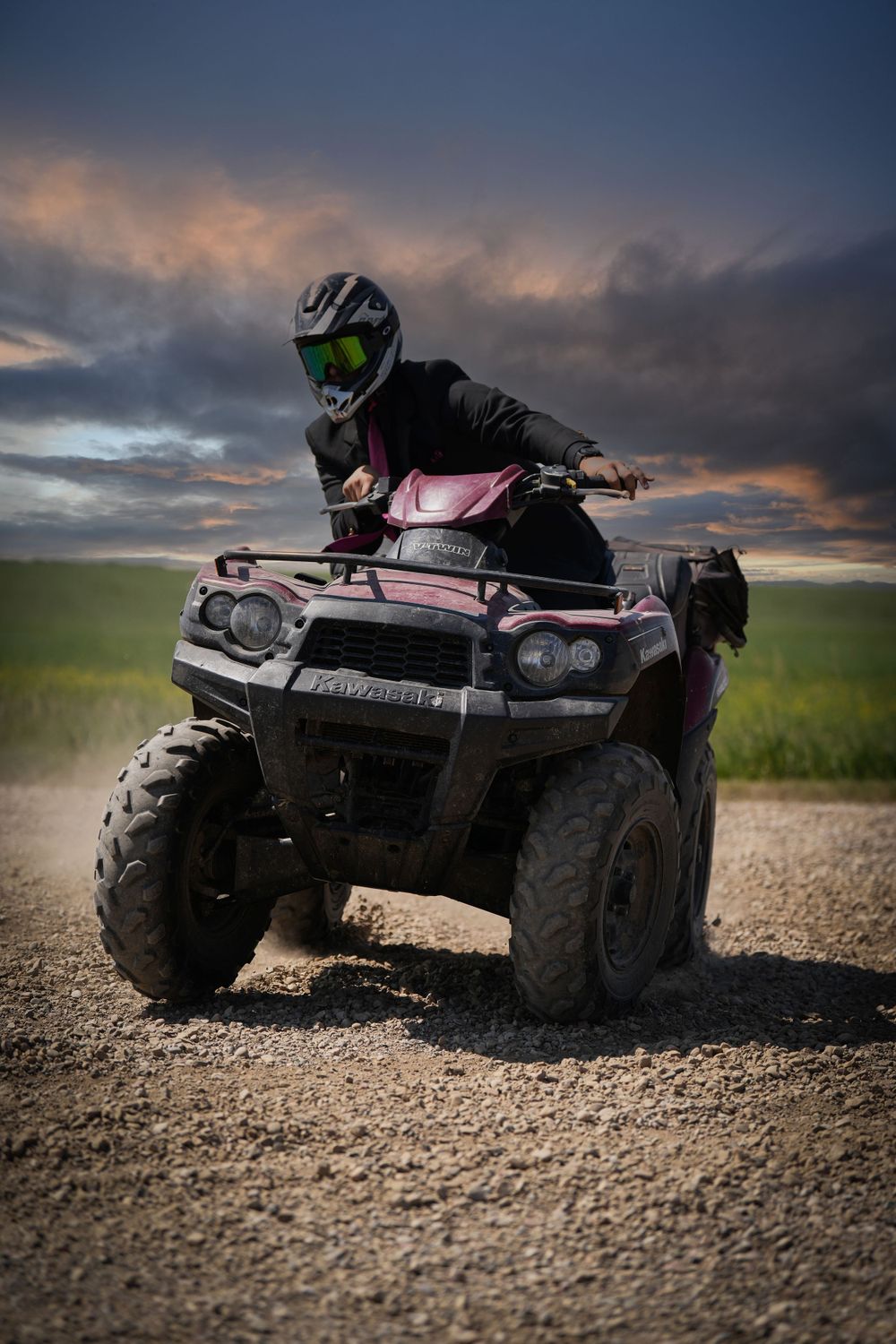 ATV rider in helmet poses with quad bike during dramatic sunset on dirt road.