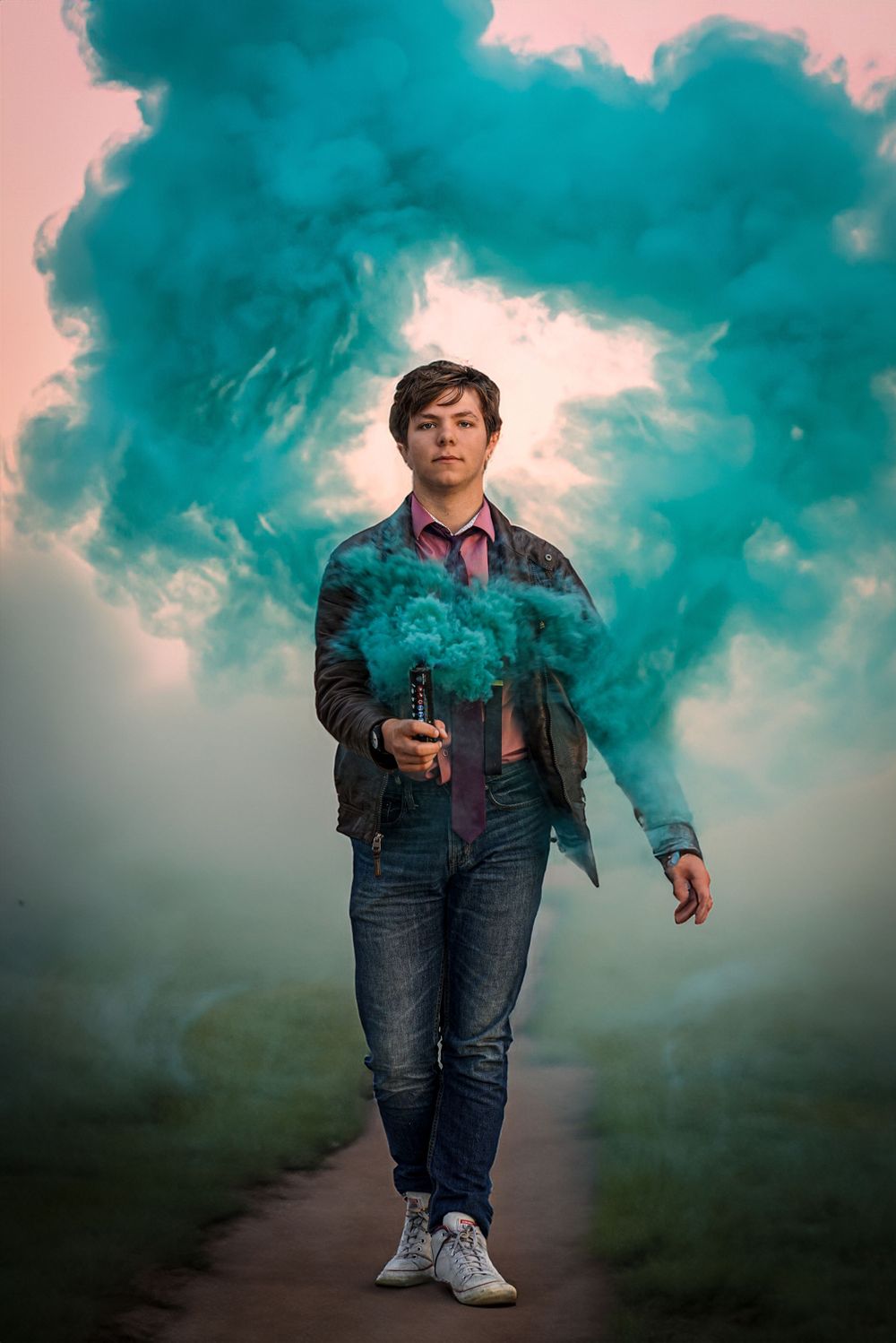 Creative portrait with teal smoke bomb effect against pink sky background.