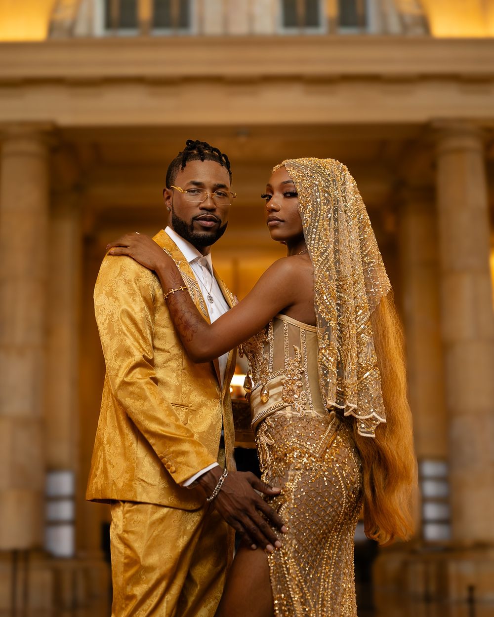 Elegant couple in sparkling gold formal wear embrace during their romantic wedding photoshoot at a grand venue.