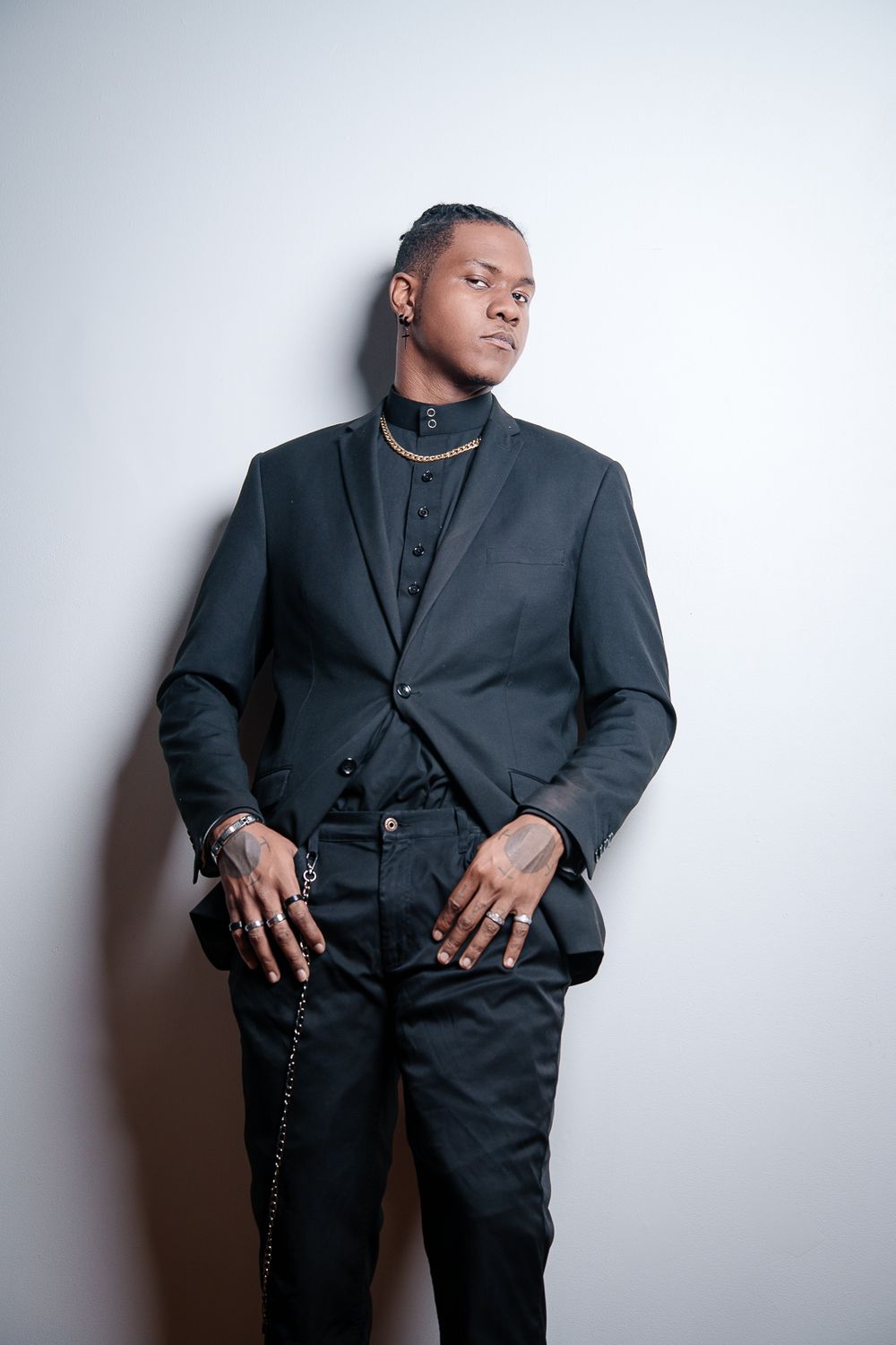 A figure in an all-black suit ensemble poses against a white wall in a series of artistic portrait shots.