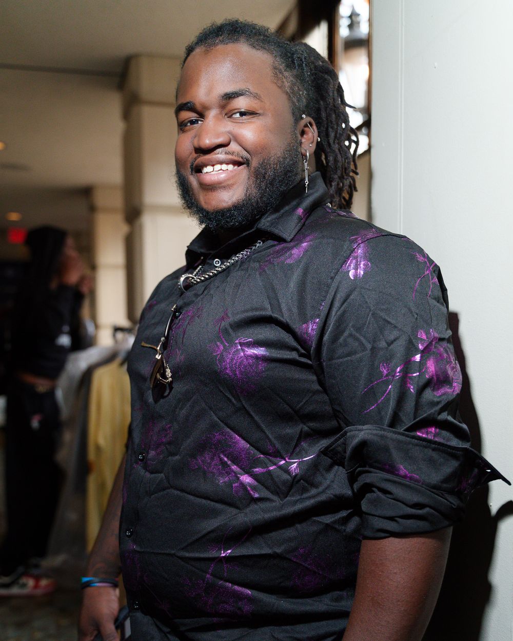Portrait of person wearing purple and black patterned shirt with dreadlocks.