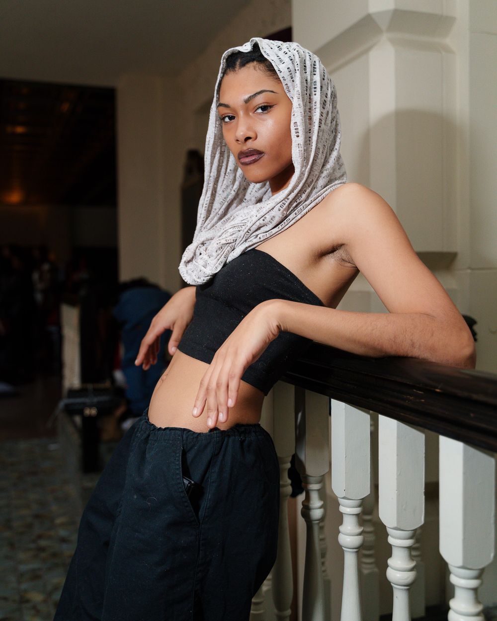 Fashion portrait of model in black tank top and silver headscarf leaning on banister.
