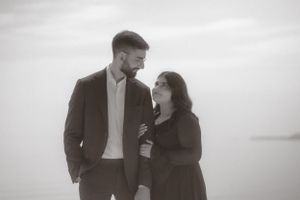 Black and white portrait of couple in formal wear standing against misty backdrop.
