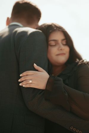 Close-up of couple embracing showing engagement ring on woman's finger.