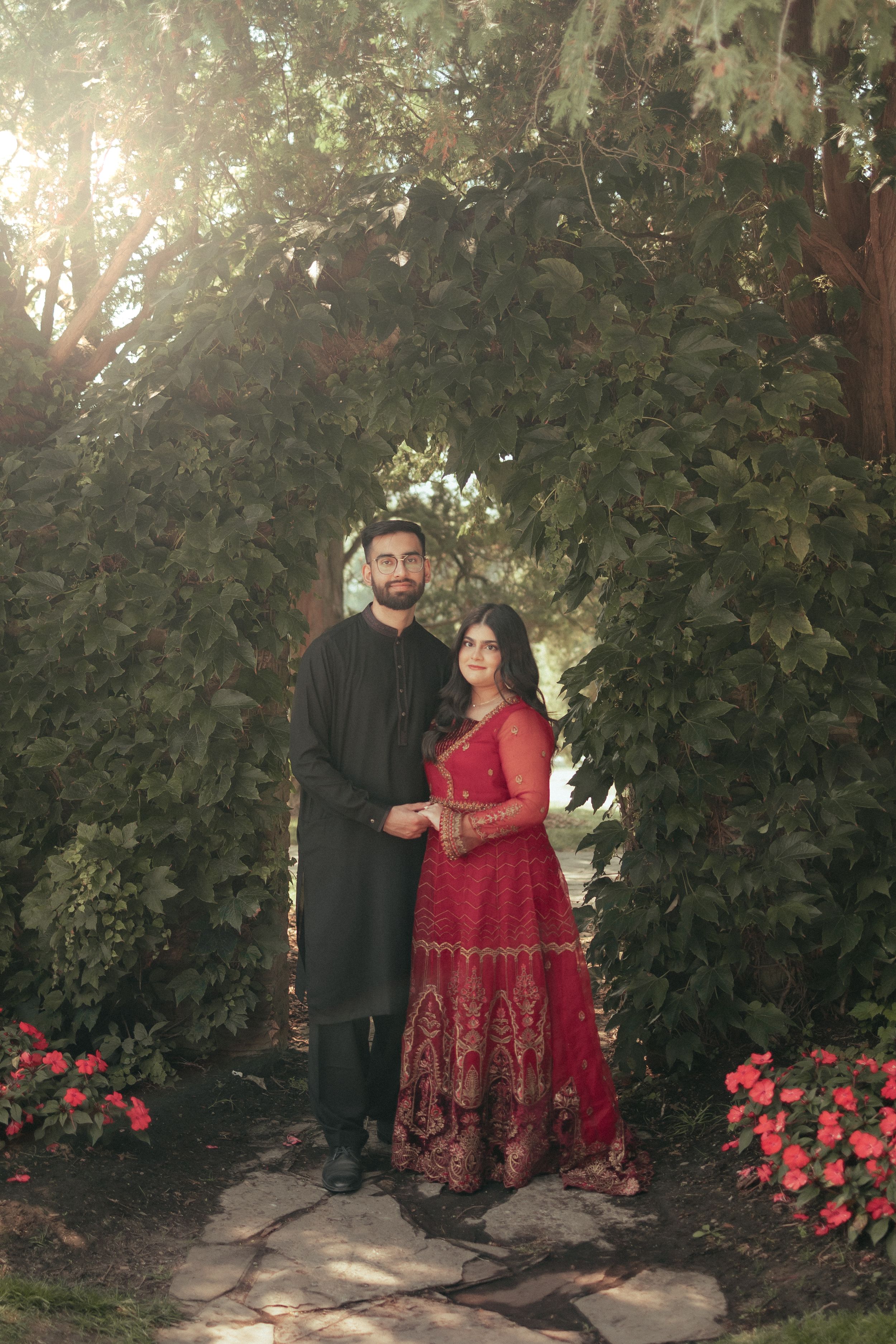 Romantic portrait of couple in traditional attire standing against garden greenery.