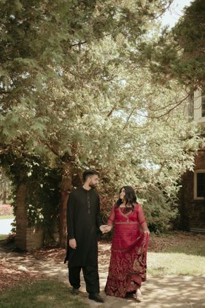 Couple walking together under tree canopy in coordinated traditional outfits.
