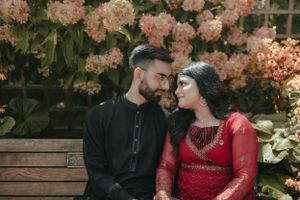 A romantic couple sits on a bench with blooming pink flowers in the background.