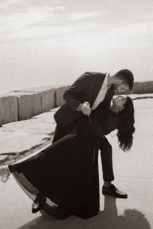 A romantic black and white photo of a couple in a classic dance dip pose by the water.