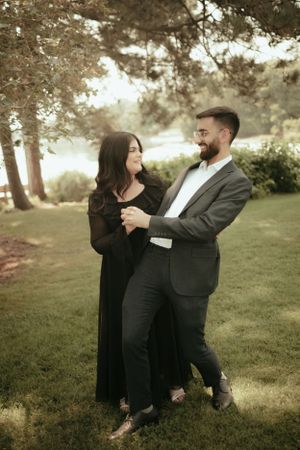 Couple dancing together on grass with trees in warm evening light.