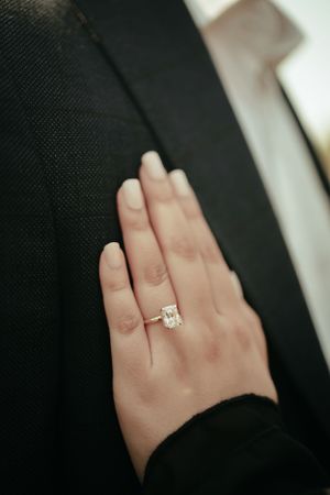 Close-up of elegant diamond engagement ring on hand against black fabric.