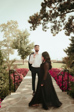 Couple on stone pathway lined with bright pink flowers and greenery.