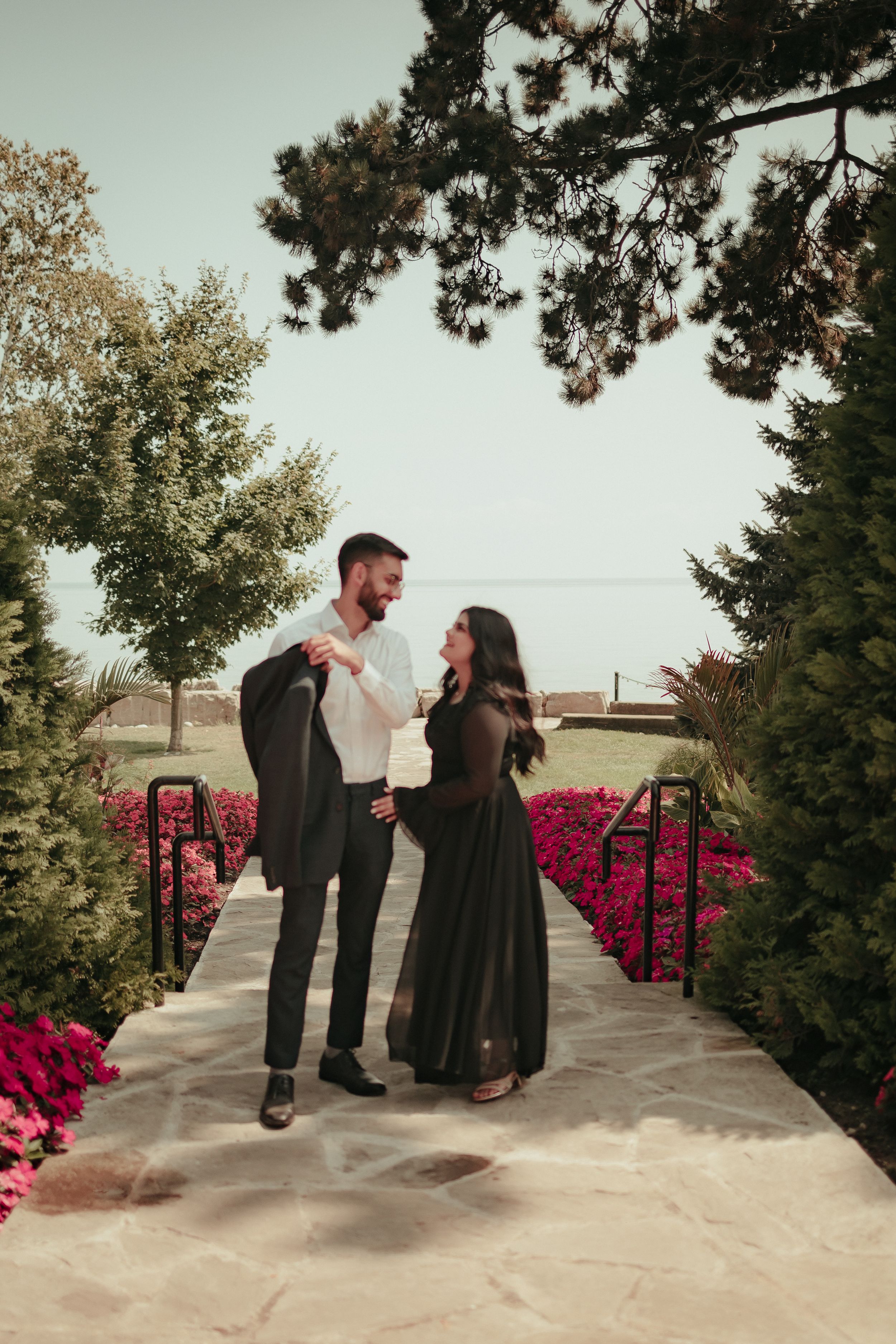 Couple sharing joyful moment on garden path surrounded by pink flowers.