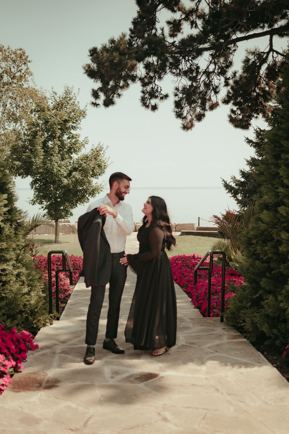 Couple sharing joyful moment on garden path surrounded by pink flowers.