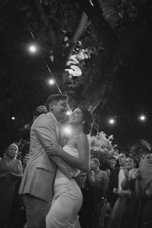 Black and white photo of a wedding couple's first dance under string lights at an outdoor reception.