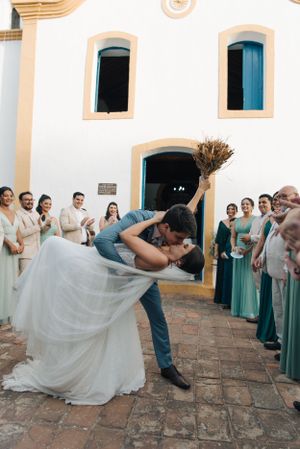 Romantic dip kiss outside church entrance as guests celebrate with sparklers.