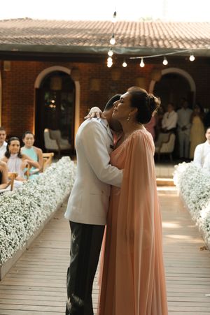 Wedding party members walk down an aisle lined with baby's breath flowers at an indoor venue.
